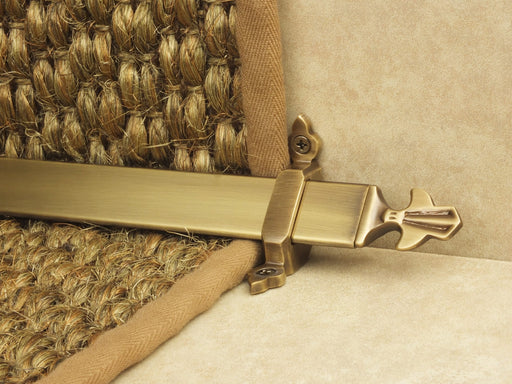 Louis design of stair rod with fleur-de-lys end, antique brass on red carpet